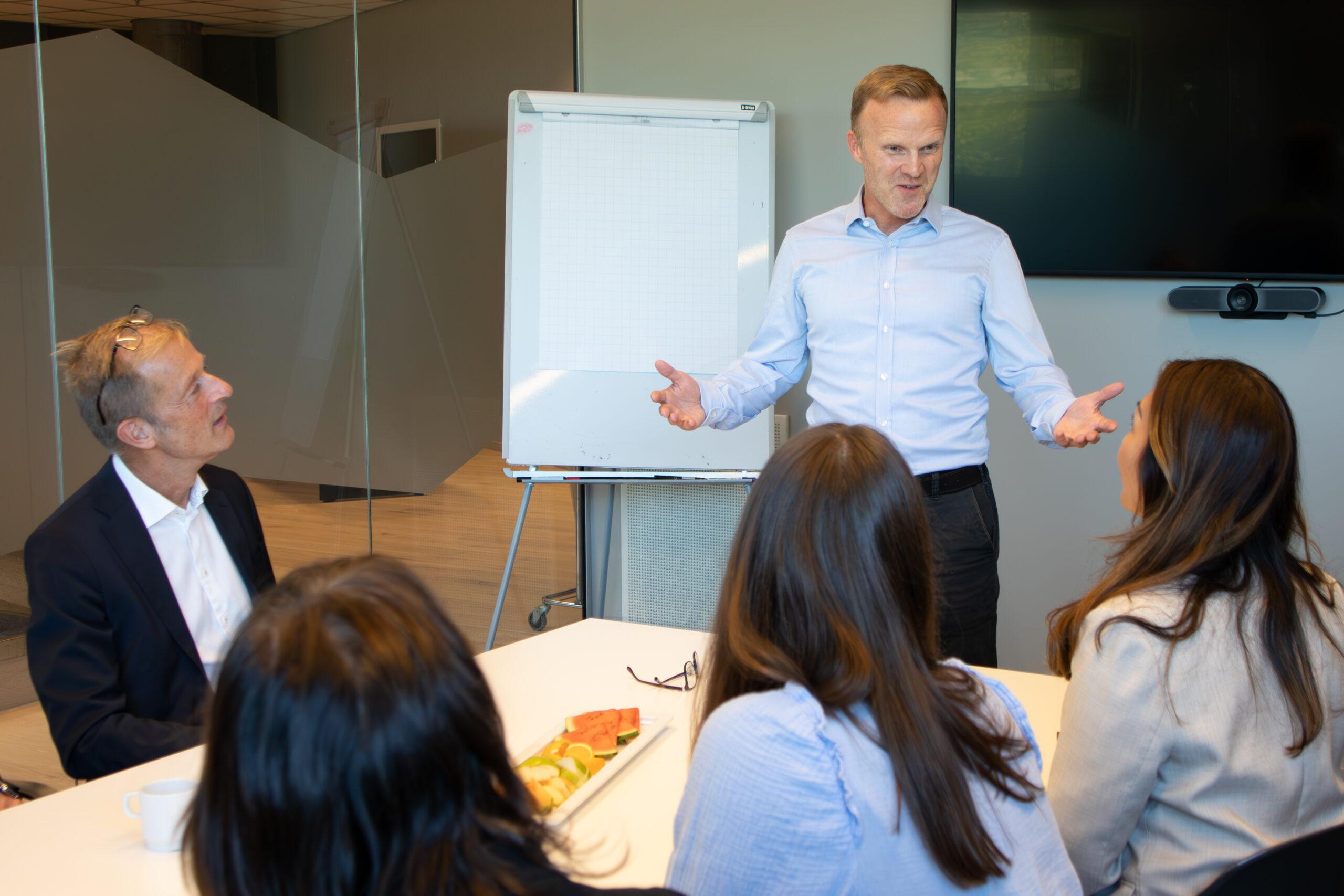 En kursholder står og snakker foran en gruppe mennesker på et salgstreningskurs.